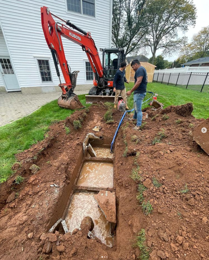 Professionals excavating septic tank in backyard with heavy equipment