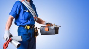 Plumber in uniform holding toolbox and tools
