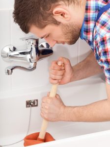 Homeowner attempting to unclog bathtub drain with plunger