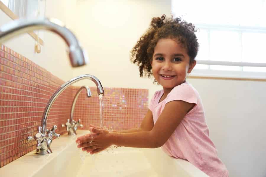 Young student washing hands in school bathroom