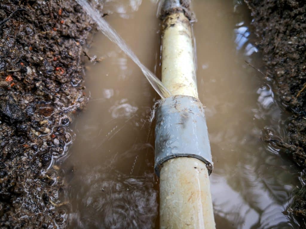 Water spraying from burst pipe in lawn