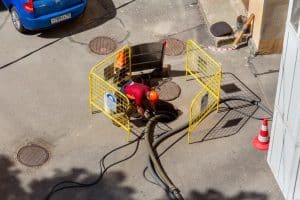 Worker crouching over open sewer hatch to perform repairs