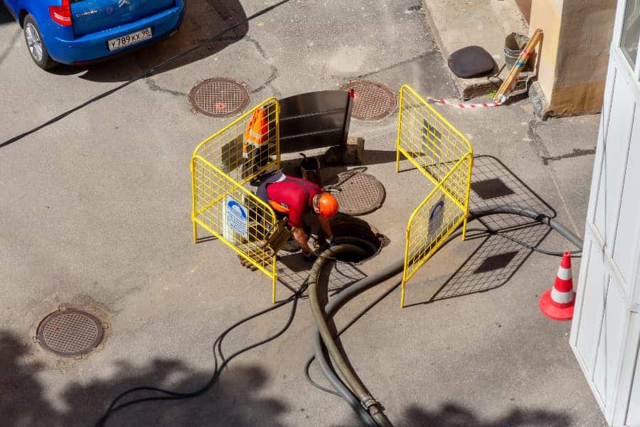 Worker crouching over open sewer hatch to perform repairs