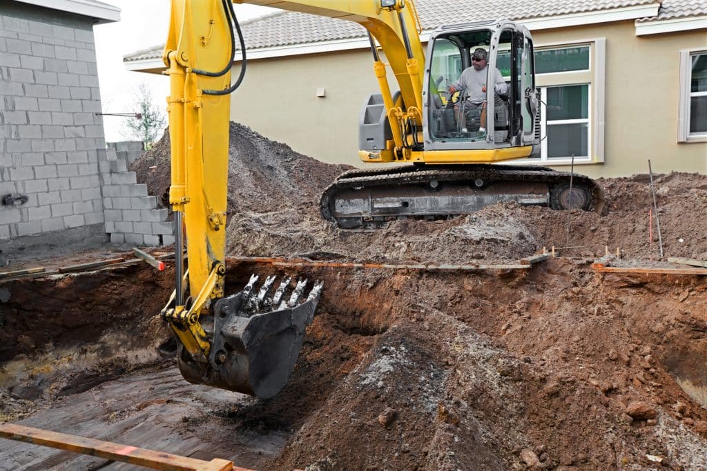 Worker using excavator to dig hole near residential home